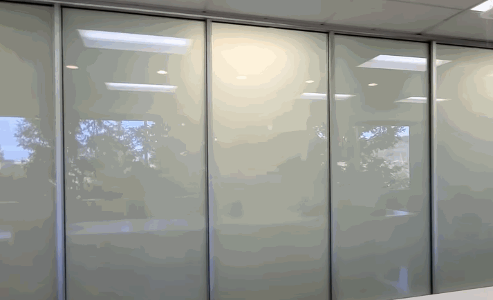 An animated view of glass panels in an office setting transitioning from transparent to opaque, demonstrating the functionality of privacy window films.